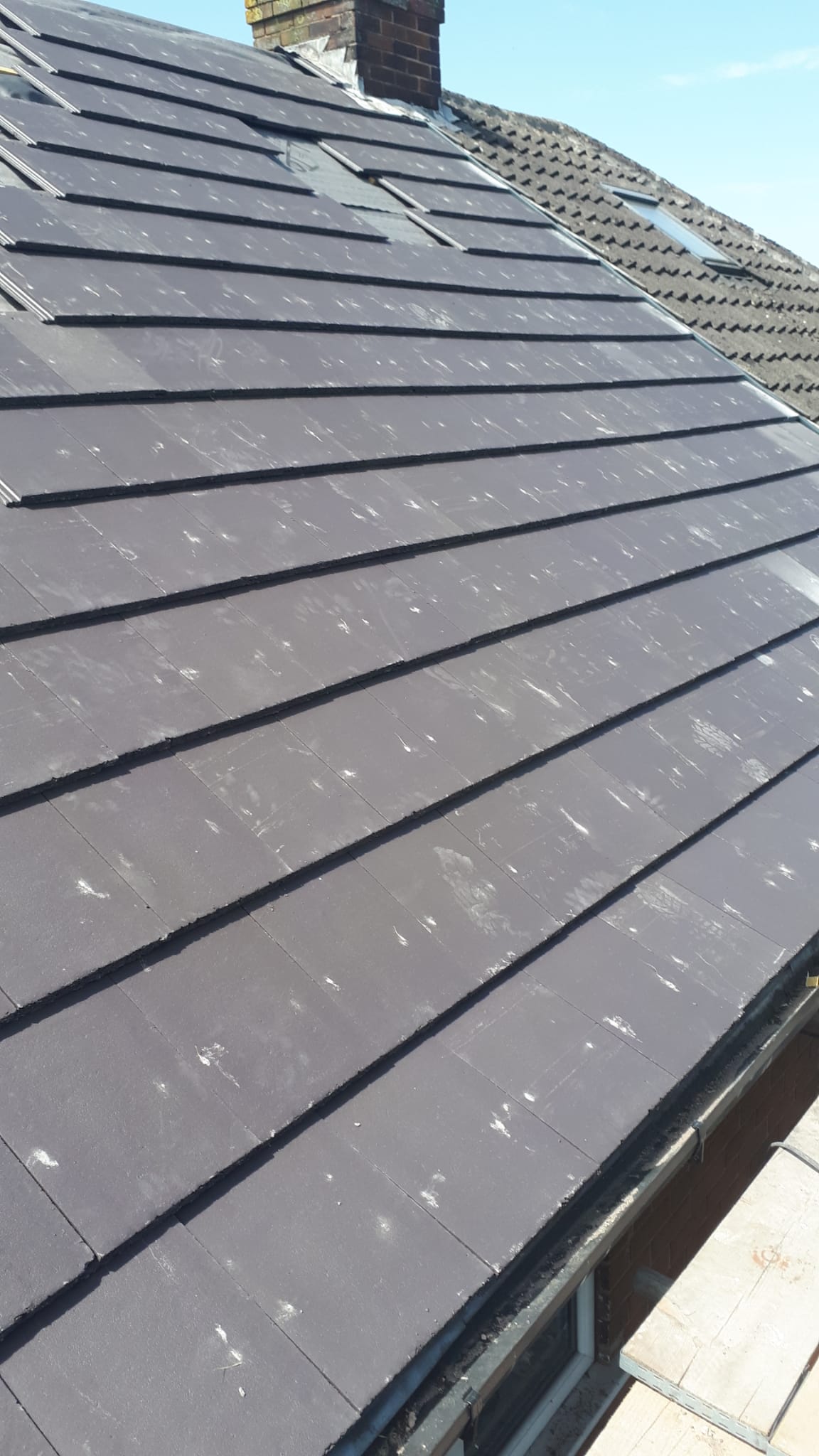 Completed new grey tiled roof against blue sky in Stoke-on-Trent