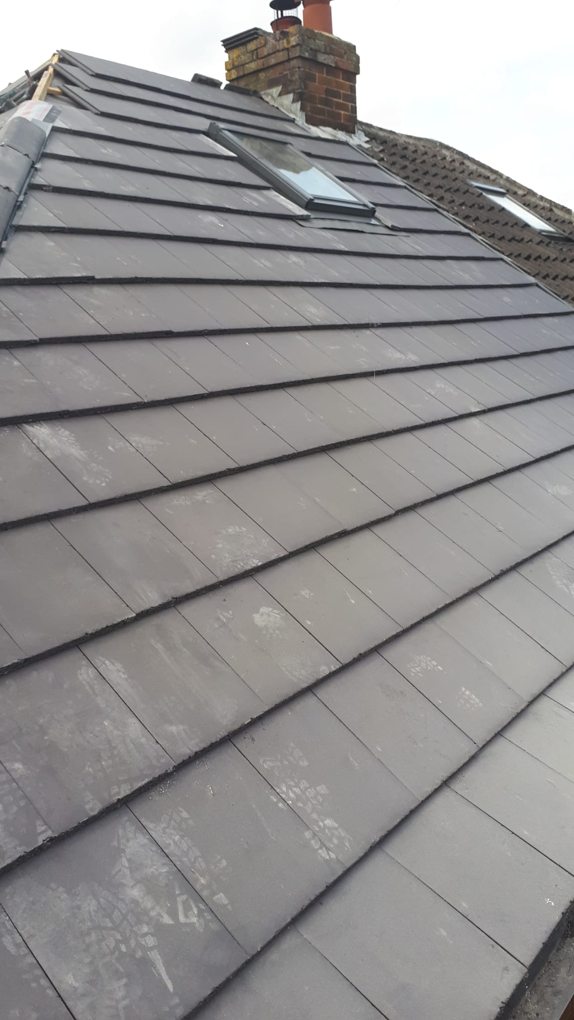 Finished grey tiled roof with skylight and chimney